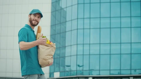 A delivery guy in Uniform Holds Paper Bag with Food Showing Thumb Up Video stock 211871813