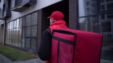 Delivery guy wearing red uniform while walking along modern buildings down city Stock Footage 144565767