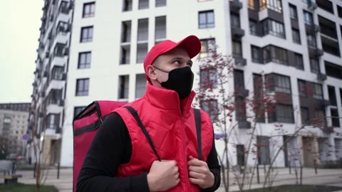 Delivery guy wearing red uniform and black mask while walking along modern Stock Footage 144567447