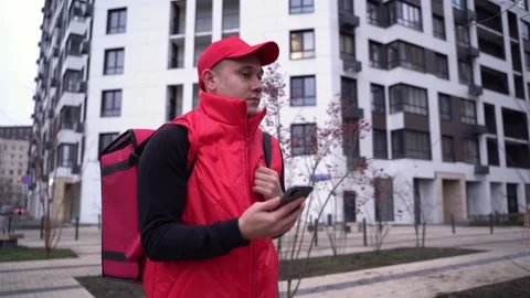 Delivery guy wearing red uniform while walking along modern buildings down city Video stock 145485256