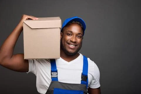 Delivery man in baseball cap holding and carrying cardboard box on his shoulder Stock Photos
