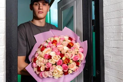 Delivery man with beautiful from multi-colored roses bouquet in the door 写真素材