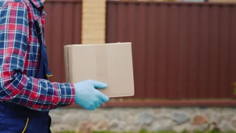Delivery man in blue uniform and medical gloves walking along fence, carryi.. Stock Footage 334698279