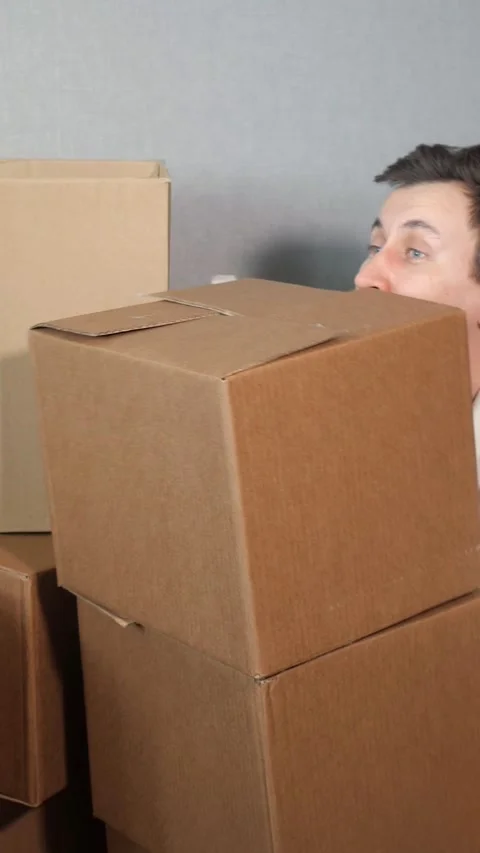 Delivery man carefully lifting and carrying a heavy cardboard box from a stack Stock Footage 341578835