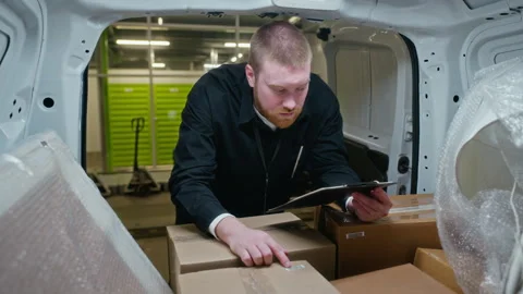Delivery Man Checking Cardboard Boxes and Writing on Clipboard in Cargo Van Stock Footage 340282691