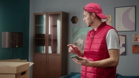 Delivery man counting boxes in new apartment and writing result in smartphone Stock Footage 149679006