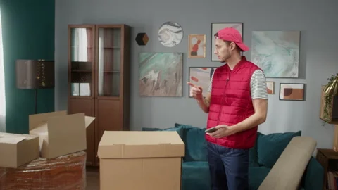 Delivery man counting boxes in new apartment and writing result in smartphone Stock Footage 150438147