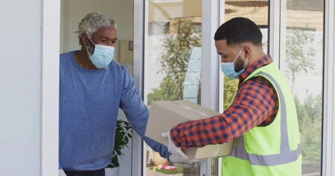 Delivery man delivering package to senior man wearing face mask at home Stock Footage