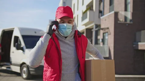 Delivery man in face mask and gloves handling parcel box, walking along the Stock Footage 166176572