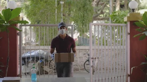 A delivery man in a face mask keeps or leaves the parcel at the gate  Stock Footage 130257069