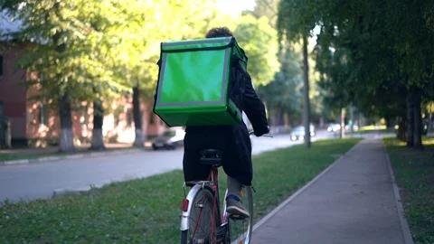 Delivery man with green backpack rides a bicycle through the city with food Stock Footage 115128607