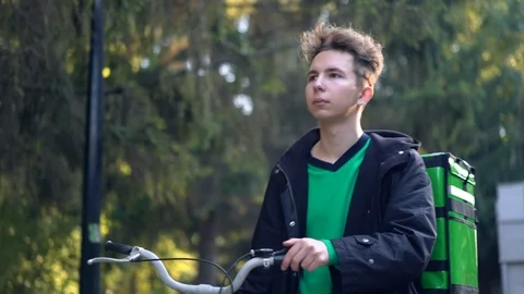Delivery man with green backpack rides a bicycle through the city with food Stock Footage 115699845