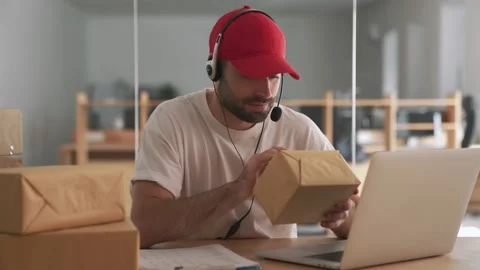 Delivery man indoors in office using laptop computer near parcel boxes Stock Footage 153843594