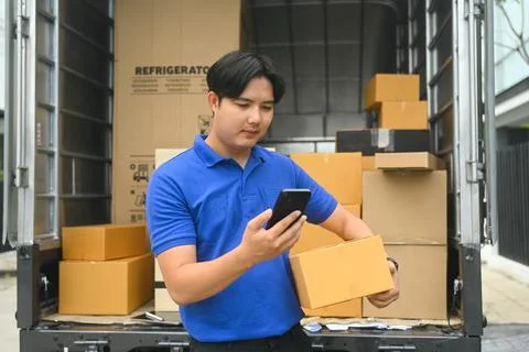 Delivery man with parcel box checking list on mobile phone while standing near Stock Photos