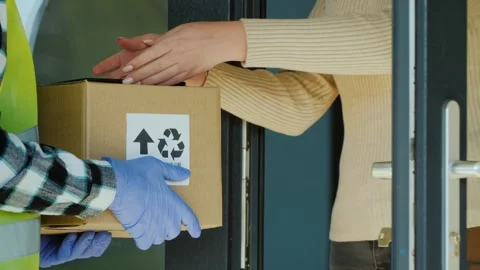 Delivery man in protective gloves giving parcel to woman at home during pan.. Видео 334993325