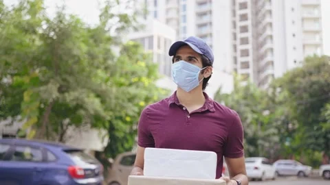 Delivery man with protective mask on face carrying parcel boxes walking on road 動画素材 167000958