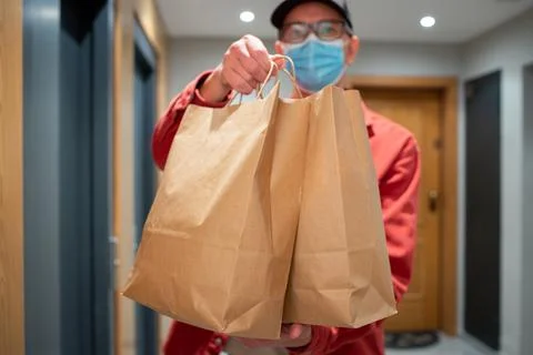 Delivery man in protective mask holding paper bag with food in the entrance. The Stock Photos
