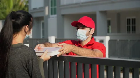 Delivery man in red uniform wearing face mask send delivering food boxes to c Stock Footage 147335143