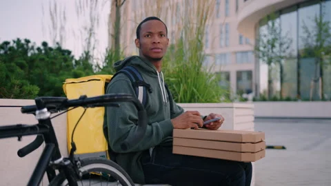 Delivery man sits on a bench with a mobile phone while waiting for a customer Stock Footage 254097803