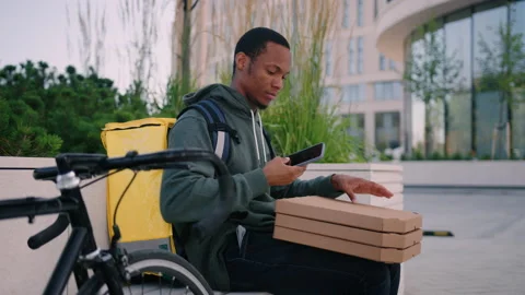 Delivery man sits on a bench with pizza boxes while waiting for a customer Stock Footage 217363151