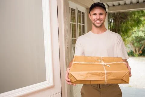 Delivery man smiling at camera offering parcel Stock Photos