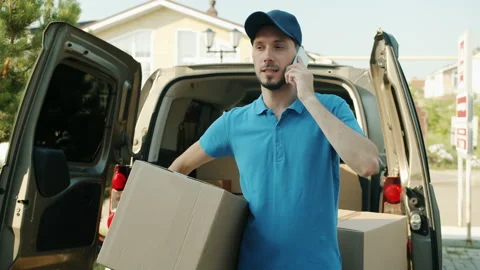 Delivery man talking on mobile phone holding parcel standing near commercial van Stock Footage 157312633