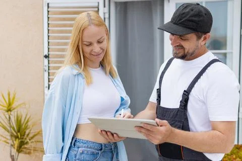 Delivery man in uniform presenting a digital contract for customer signatur.. Stock Photos