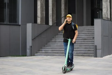 Delivery man using smartphone and riding push scooter in the city. 스톡 사진
