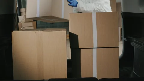 Delivery man wearing protective suit unloading parcel boxes from car trunk .. Stock Footage 334838792