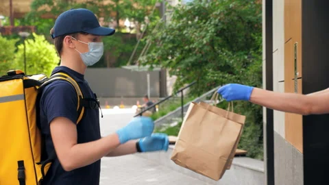 Delivery man wears protective medical face mask and gloves picks up paper bag Stock Footage 157443900