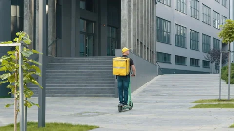 Delivery man with yellow backpack rides a electric scooter through the city with Stock Footage 172016788