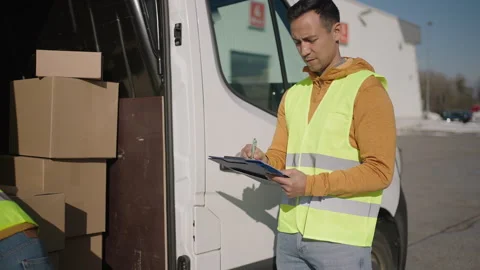 Delivery men standing by the van, one loading boxes while other checks the list  Stock Footage 263895197