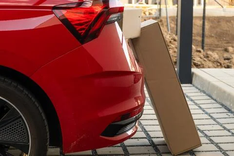 Delivery package positioned next to red automobile parked in contemporary Foto stock