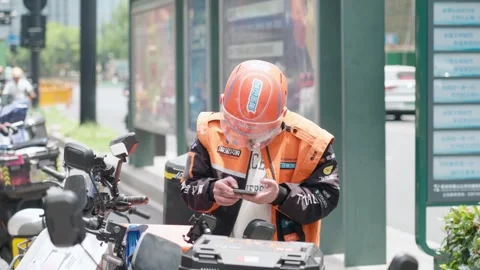 Delivery rider checking his phone for next gig in Hangzhou, China, representing Stock Footage 335995754