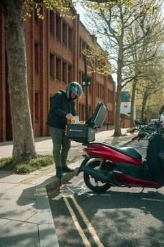 Delivery rider checking orders on red scooter in Chiswick Stock Photos