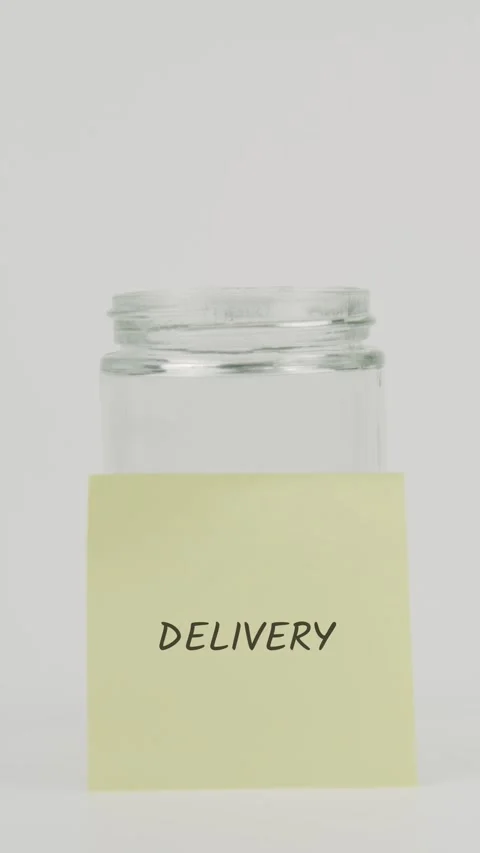 Delivery text or word on yellow sticky note attached to glass jar with hand Stock Footage 311712138