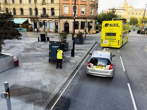 Delivery worker with Amazon box on a Manchester street beside a bright Slic.. Stock Photos