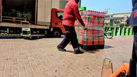 A delivery worker in Dubai pulls a pallet of bottled drinks, tightly secured Stock Photos