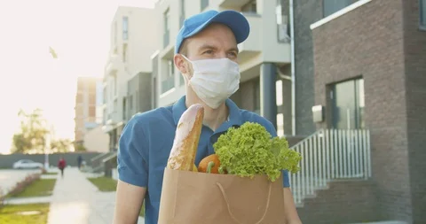 Delivery worker wearing blue cap and medical mask walking street, carrying Stock Footage 129557881