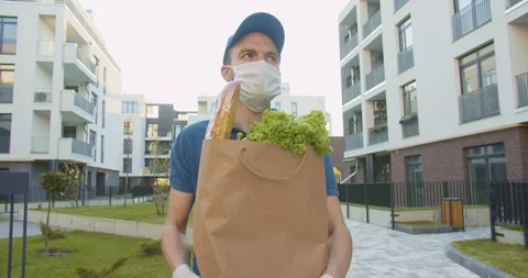 Delivery worker wearing blue cap and medical mask walking street, carrying Stock Footage 129679457