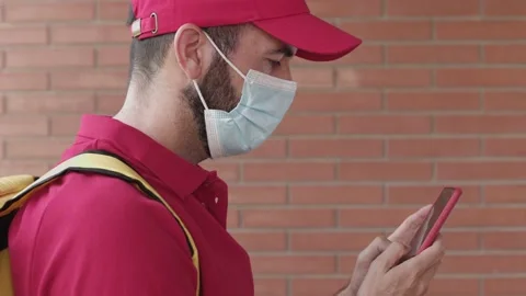 Delivery young man in protective man wearing red uniform using smart phone Stock Footage 159514985