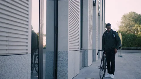 Deliveryman with a backpack walks next to a bicycle and pulls out a mobile phone Stock Footage 222892265