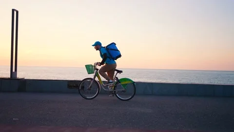 A deliveryman in a blue uniform with a backpack on a bicycle is in a hurry Stock Footage 236915747