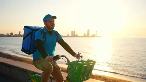 A deliveryman in a blue uniform with a backpack of food goes on a bicycle Stock Footage 237310331