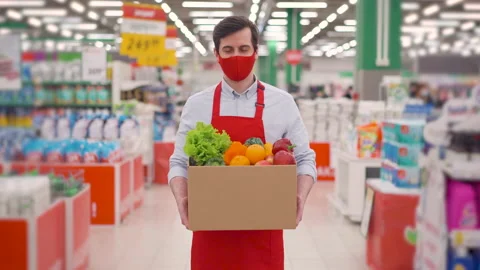 Deliveryman in face mask and uniform standing in supermarket with vegetables in Stock Footage 147995000