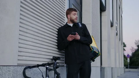 The deliveryman spends time on the phone while waiting for new orders outside Stock Footage 219459707