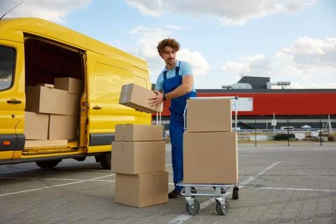 Deliveryman stacking parcel boxes into trolley cart providing courier service 写真素材
