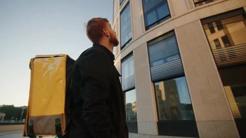 A deliveryman with a yellow backpack rides up to the building on a bicycle Stock Footage 219461384