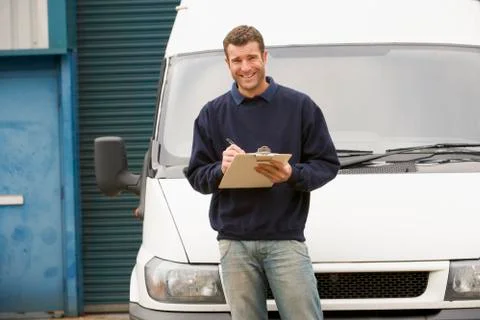 Deliveryperson standing with van writing in clipboard smiling Stock Photos