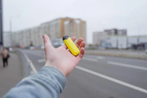 Demonstratively extends his hand with a bright yellow electronic cigarette 写真素材